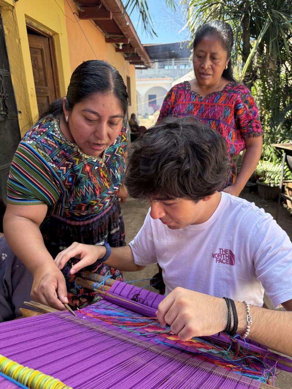 Craft and Design student Juan Diego Ocharan is taught how to use a traditional back strap loom by two local women in the village of San Antonia Agua Caliente.