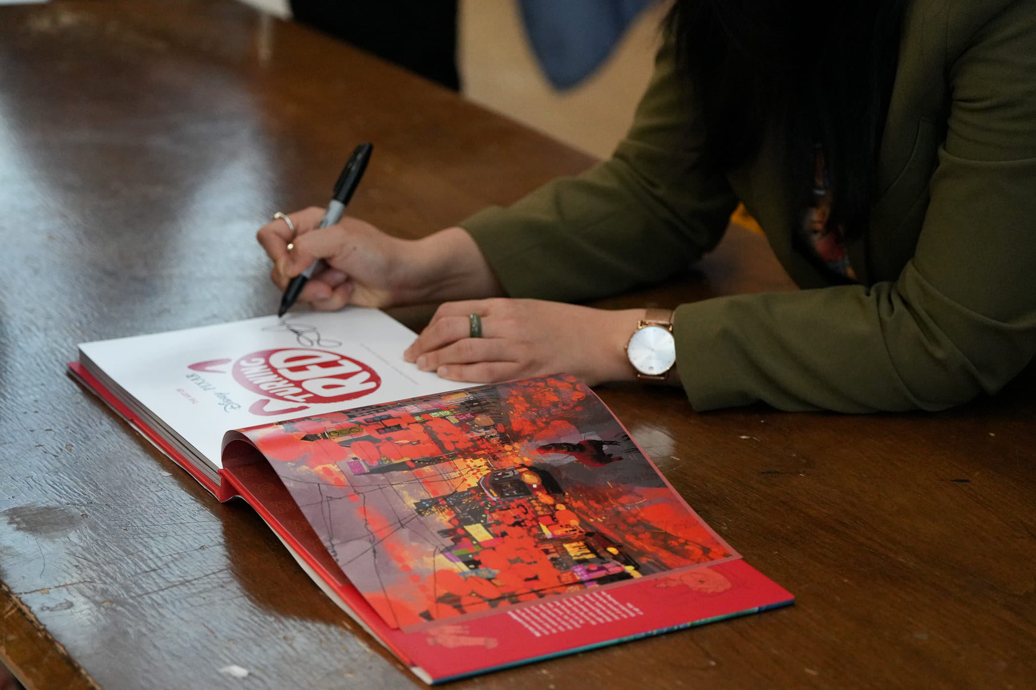 A close-up of Domee Shi signing a copy of The Art of Turning Red