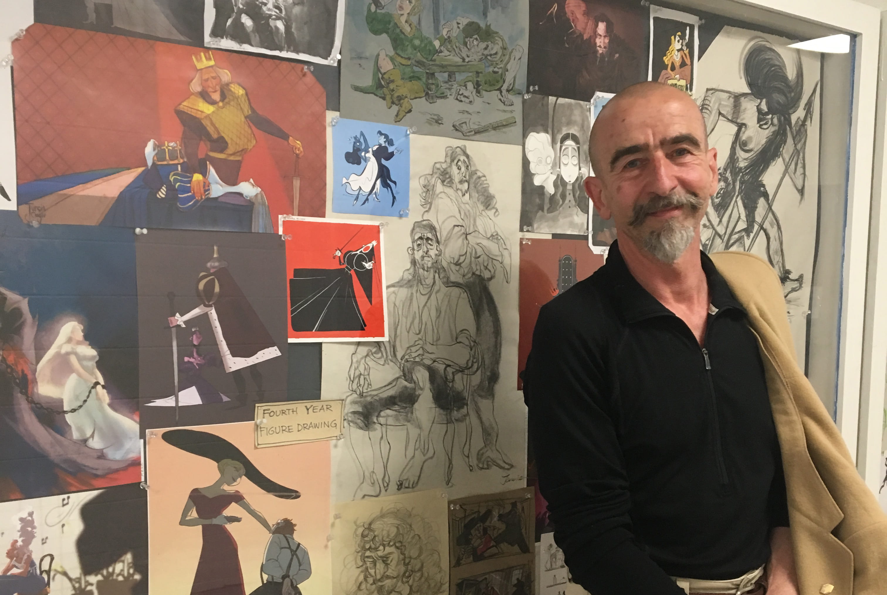 Life drawing model Ed standing in front of a display case of illustrations in a hallway at Sheridan