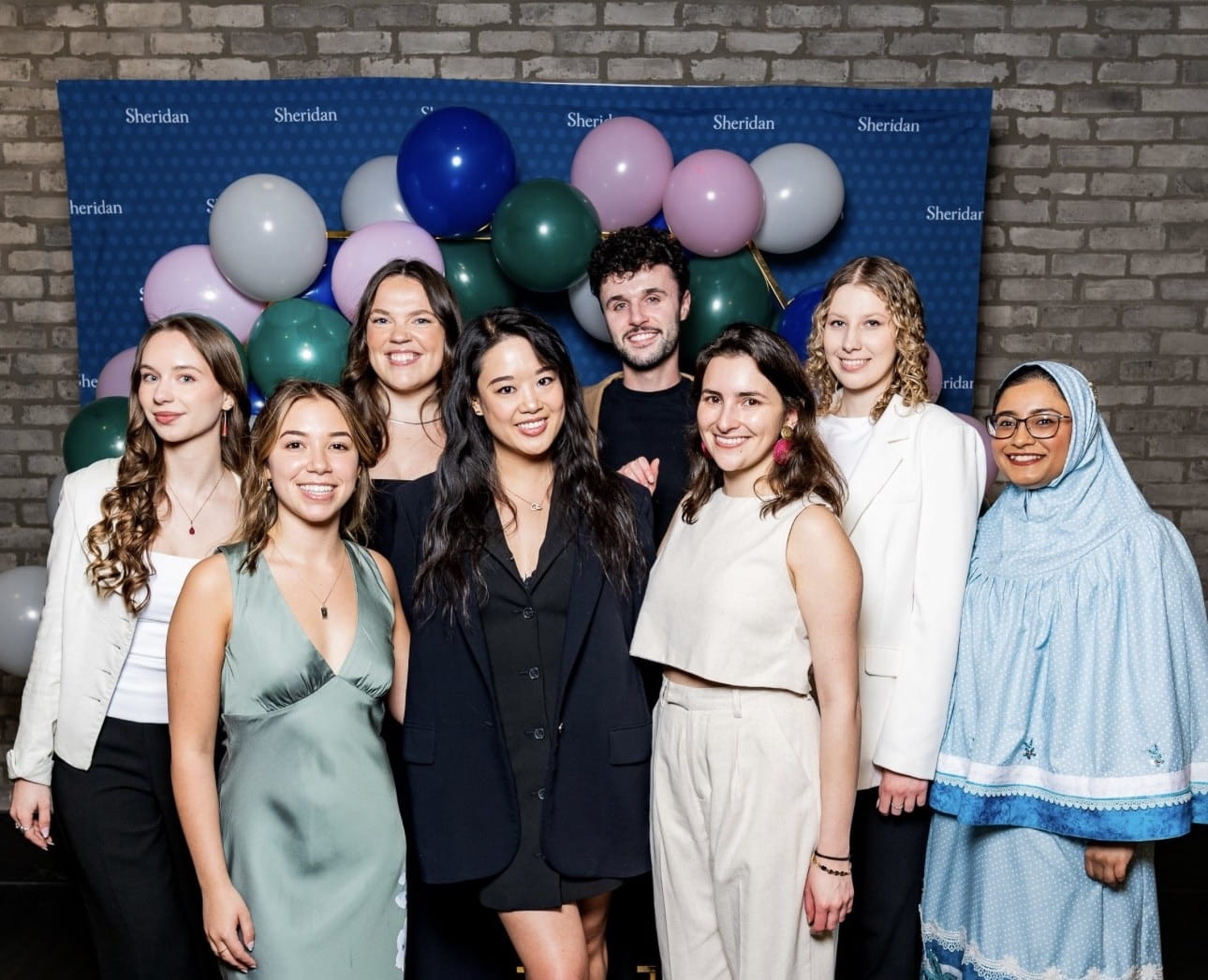 Francesca Mak stands with fellow Interior Design students in front of a Sheridan backdrop and balloons