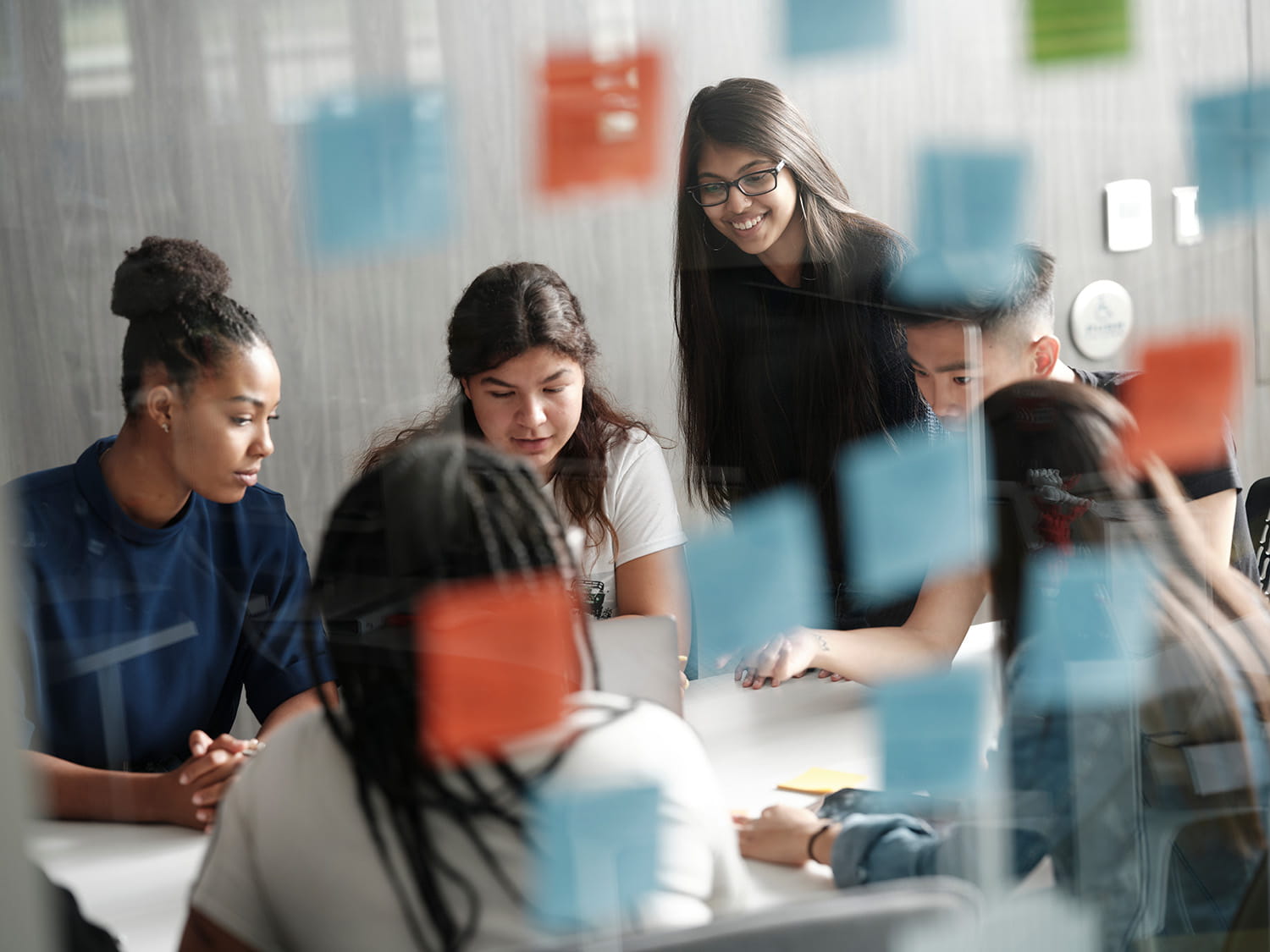 Business students gathered around a table with post-it notes in the foreground on a glass wall