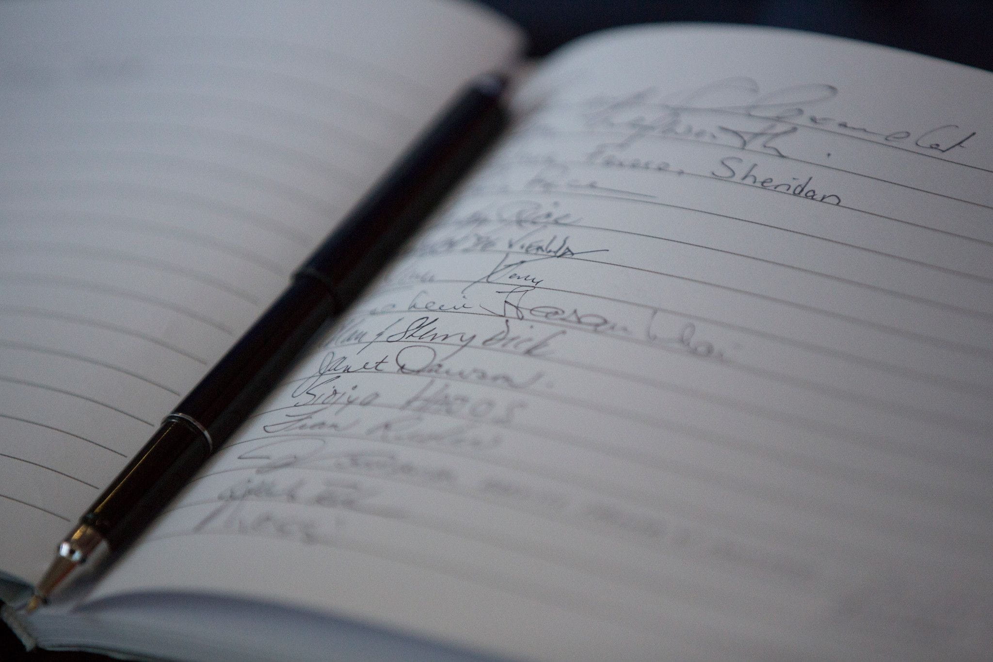 A close-up of an open notebook. A black and silver pen is placed in the middle, sitting in the book's binding.