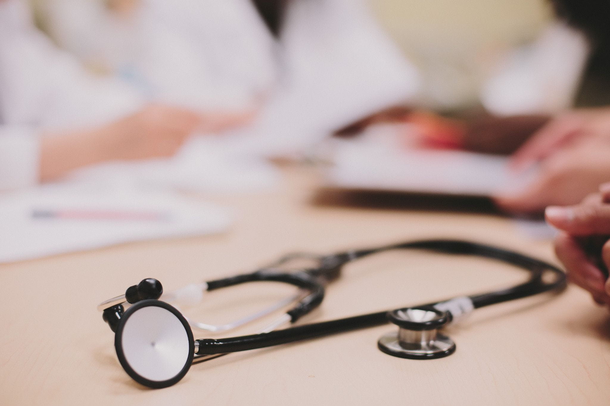A stethoscope on a table with a blurred group of people in lab coats in the background
