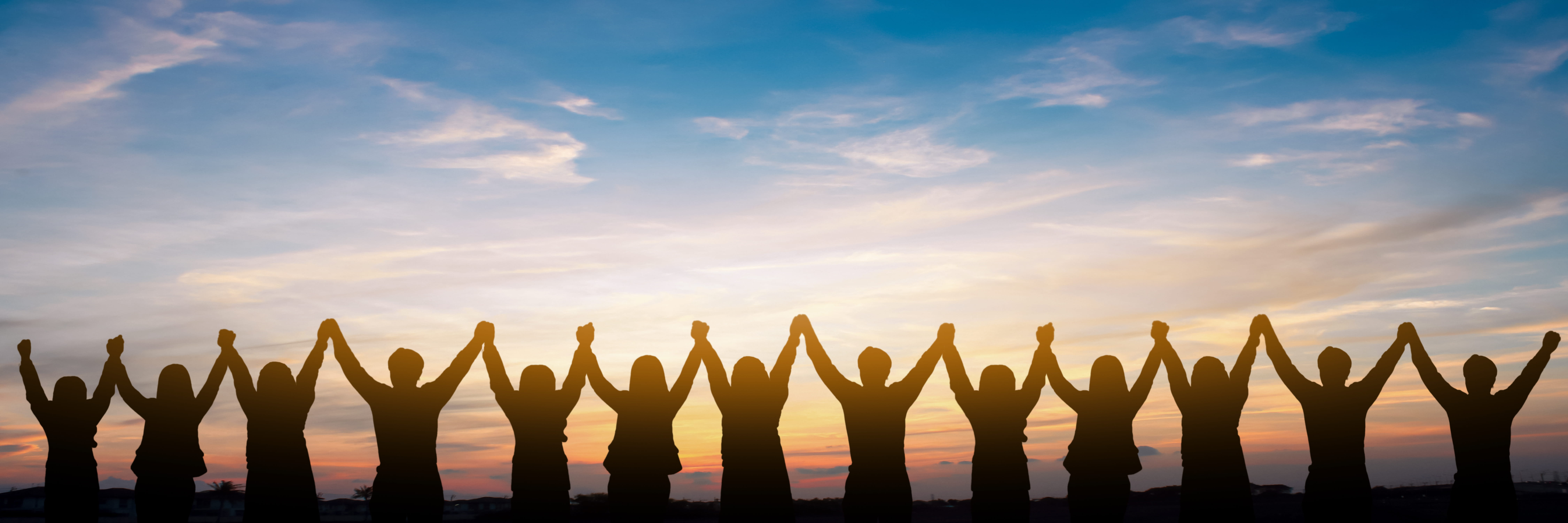 Silhouettes of people holding hands with their arms raised in the air and a sunset in the background