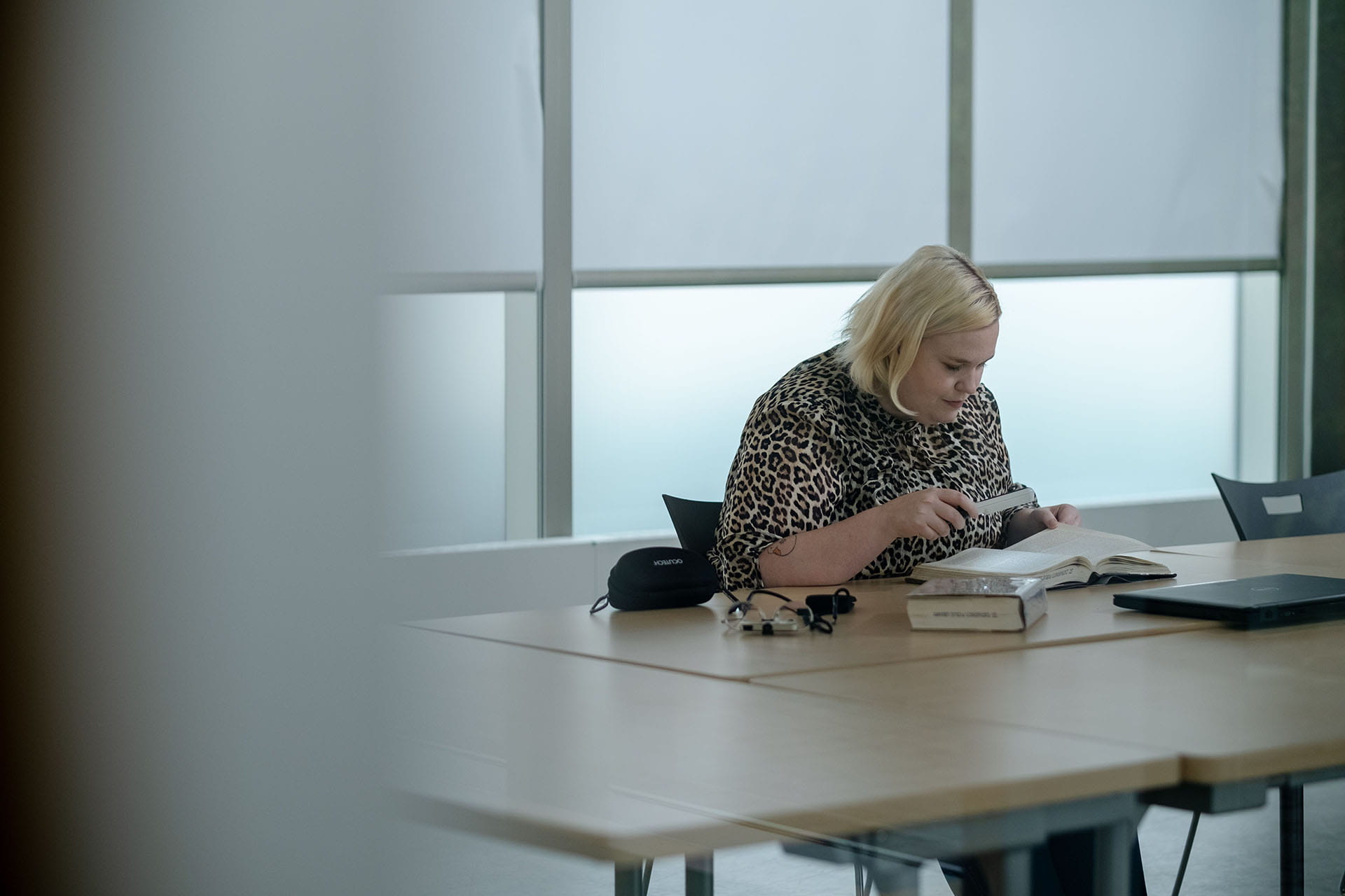 Person seated at a table using an assistive device to read a textbook.