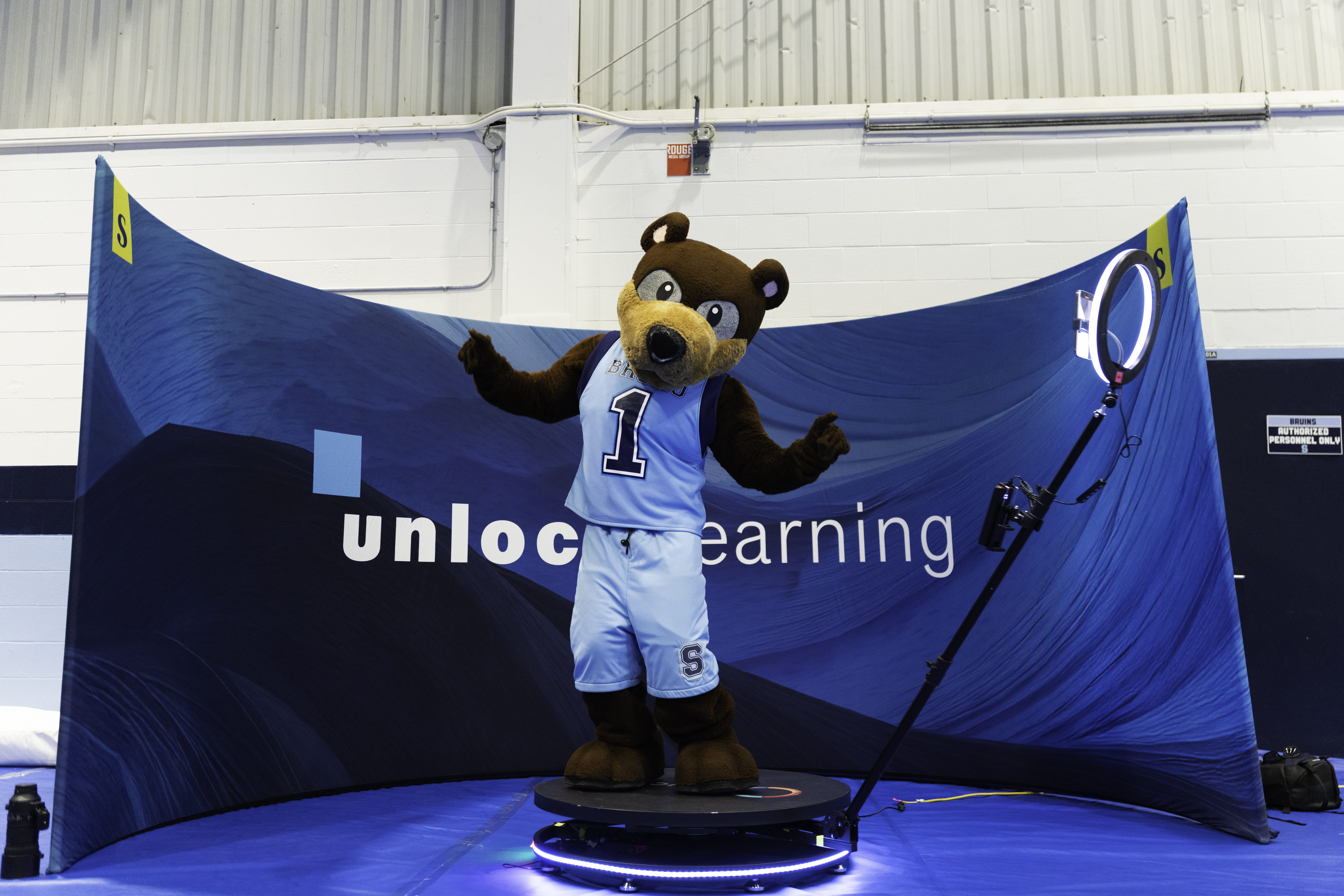 Bear mascot Bruno stands in front of a blue banner that says unlock learning.