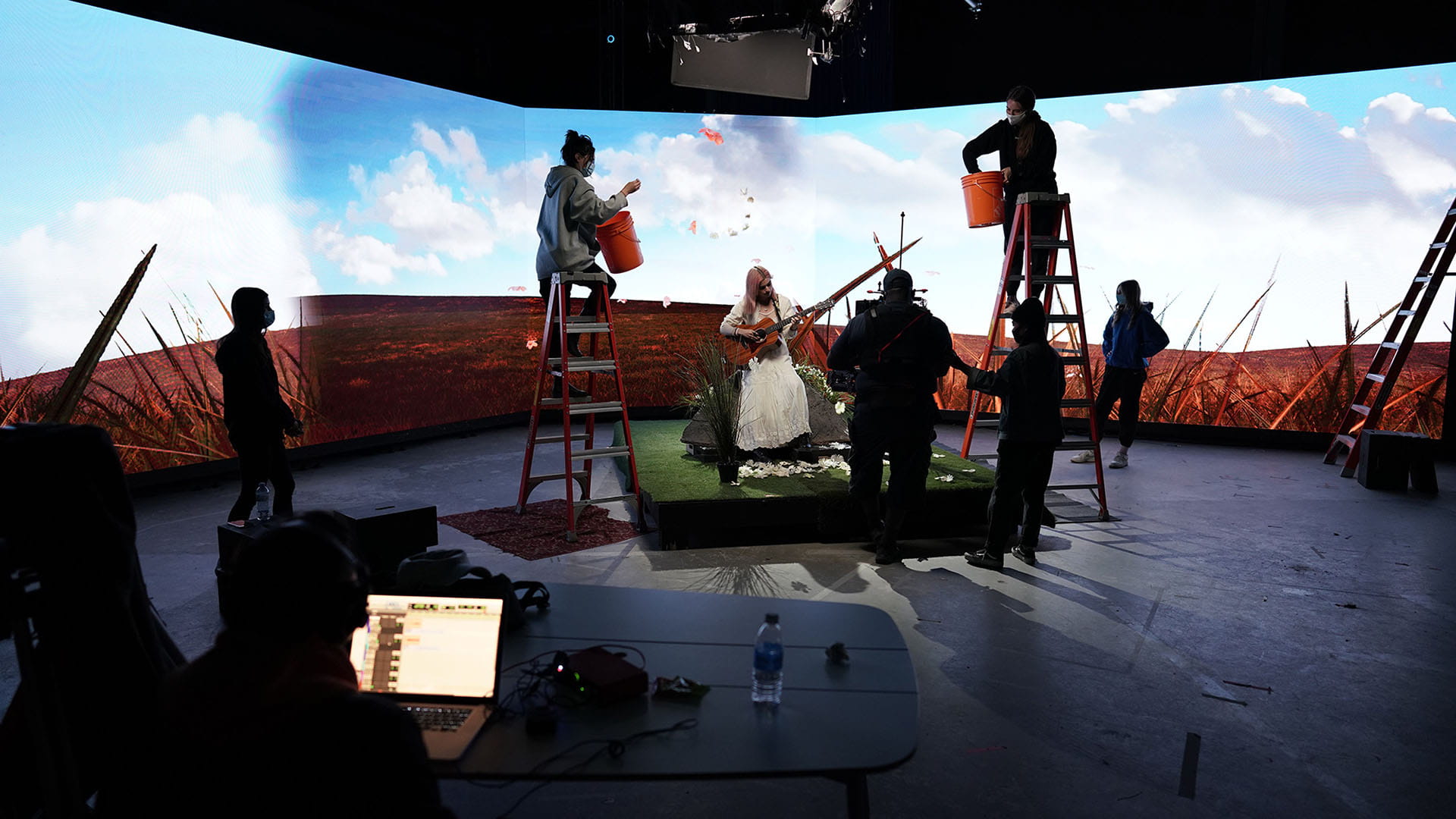 Students on ladders throw props into a camera shot of a musical performance.