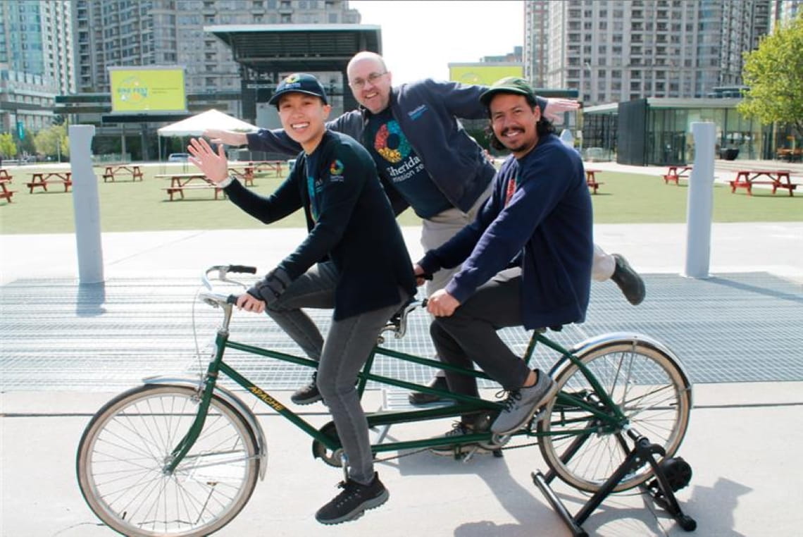 Three people from Sheridan 任务零 pose with a tandem bike on campus