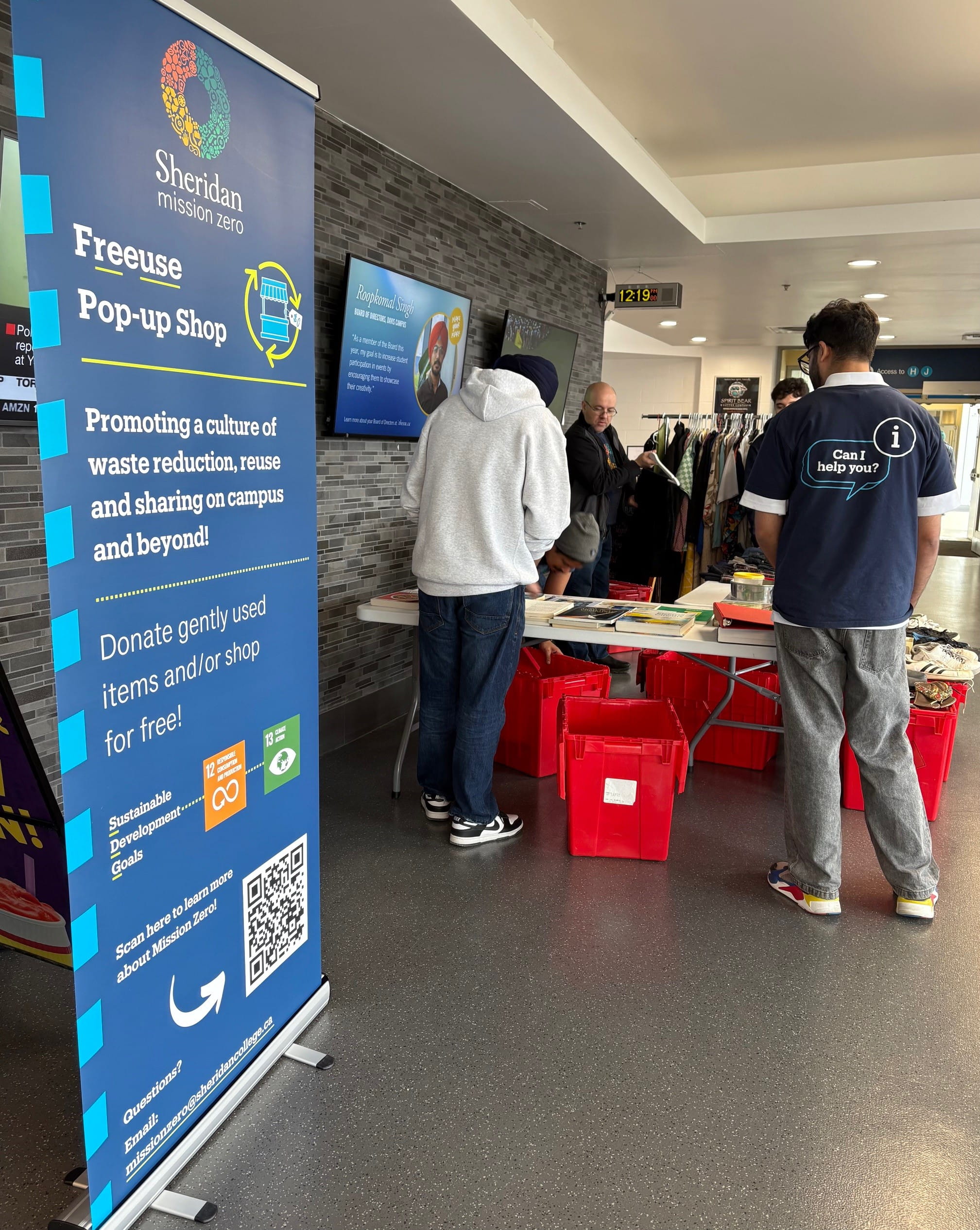 A poster which says Freeuse Pop-Up Shop in front of a table with free items as people gather to look.