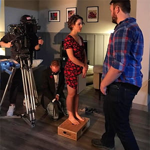 ATVF students working on a film set. An actor stands on a box in front of the camera.