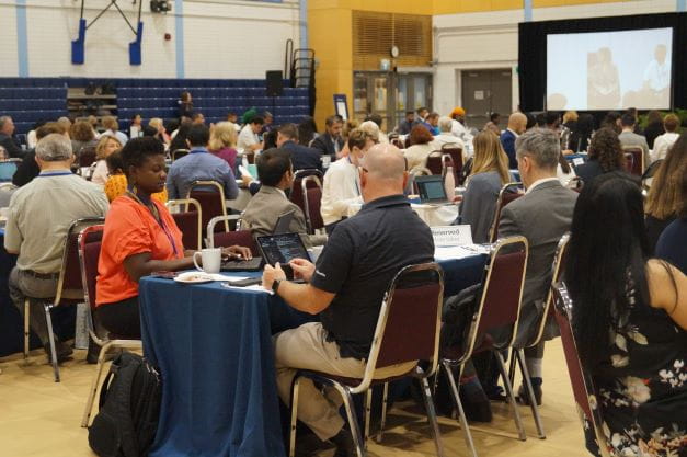 A room full of people sitting at tables in a gymnasium