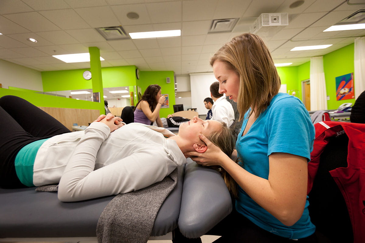 Person sitting behind another person lying on a treatment bed in a clinical setting at Sheridan
