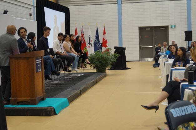 A group of students sit on stage in front of audience